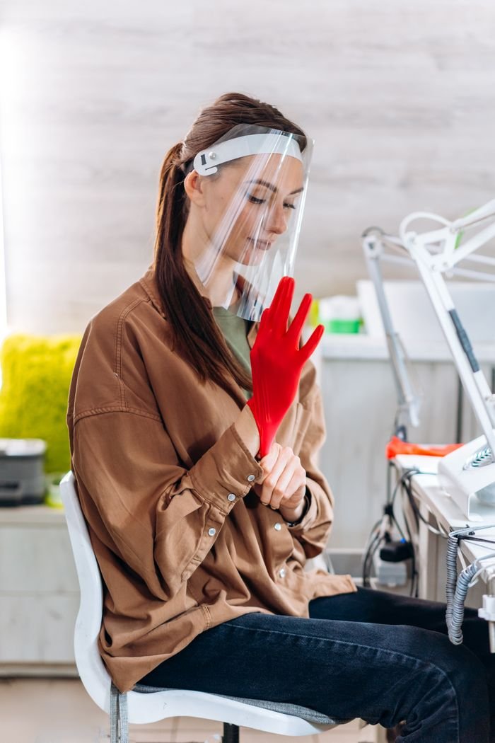Mastering the First Impression: Your intriguing post title goes here Adult woman sitting indoors wearing a face shield and red glove, engaged in a task.